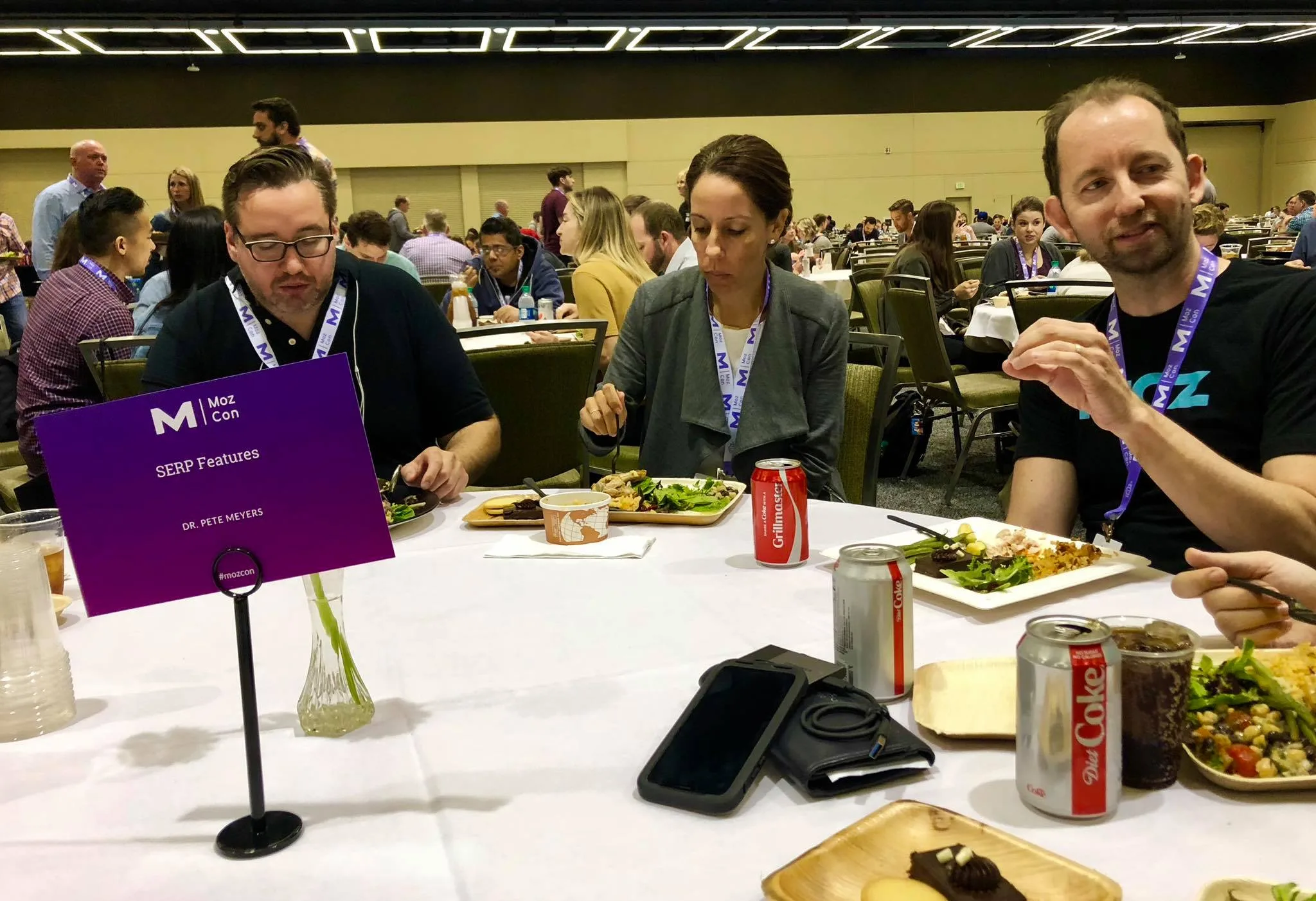 A lunch table at MozCon with a card reading "SERP Features, Dr. Pete Meyers," three attendees eating and talking around it.