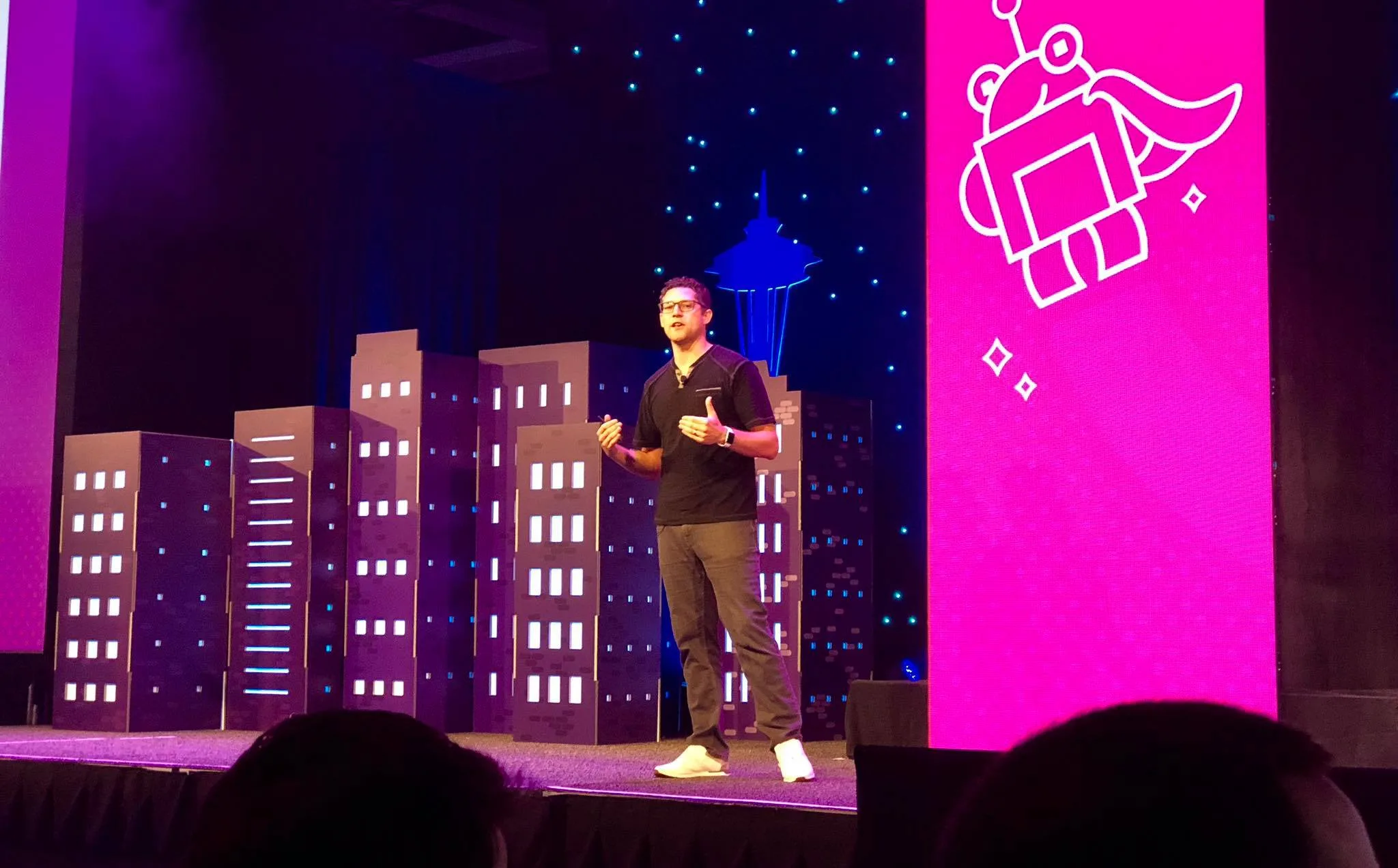 Mike Ramsey on the MozCon stage, beside a large screen displaying the conference's caped robot mascot graphic.